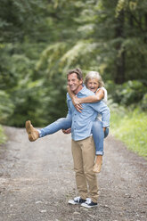 Senior man giving his wife a piggyback ride on forest track - HAPF01075