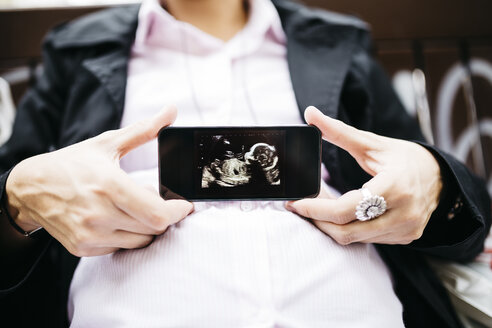 Schwangere Frau zeigt Ultraschallbild auf Handy - JRFF01009