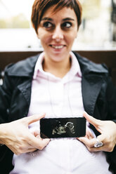 Pregnant woman showing ultrasound image on cell phone - JRFF01010