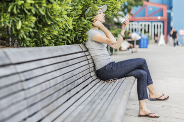 Frau sitzt auf einer Bank und benutzt einen Taschenspiegel - GIOF01599