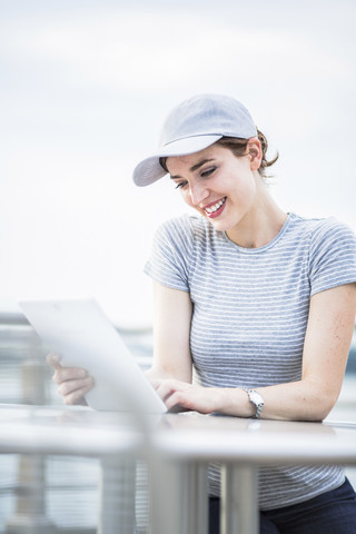 Lächelnde Frau mit Basecap schaut auf Tablet, lizenzfreies Stockfoto