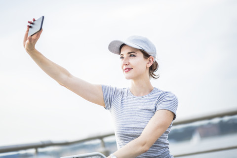 Frau mit Basecap macht Selfie mit Handy, lizenzfreies Stockfoto