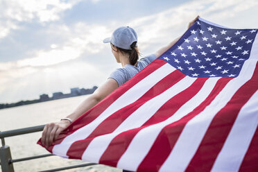 Rückenansicht einer Frau mit Basecap, die eine amerikanische Flagge hält - GIOF01611