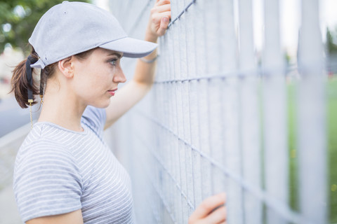 Frau mit Basecap schaut durch den Zaun, lizenzfreies Stockfoto