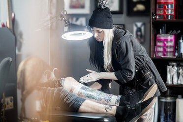 Female tattoo artist applying protective wrap on finished tattoo - ZEF11599