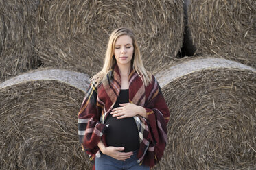 Schwangere Frau mit geschlossenen Augen vor Strohballen stehend - HAPF01096