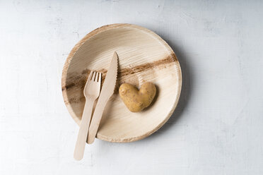 Potato in heart shape and wooden fork and knife on palm leaf plate - MYF01837