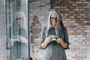 Lächelnde Frau mit langen grauen Haaren hält Kamera - KNSF00438