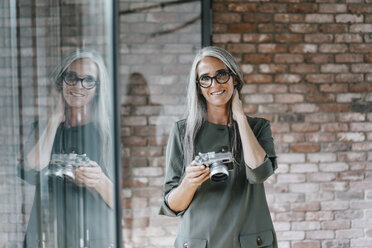 Porträt einer lächelnden Frau mit langen grauen Haaren, die eine Kamera hält - KNSF00446