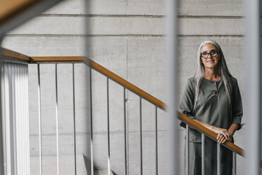 Portrait of smiling woman with long grey hair in staircase - KNSF00458