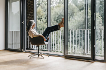 Woman with long grey hair sitting on chair at the window - KNSF00471