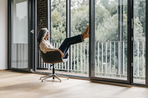 Frau mit langen grauen Haaren sitzt auf einem Stuhl am Fenster - KNSF00471
