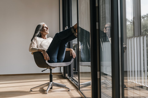 Frau mit langen grauen Haaren sitzt auf einem Stuhl am Fenster, lizenzfreies Stockfoto