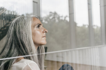 Woman with long grey hair looking out of window - KNSF00475
