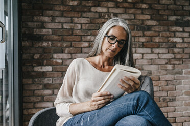 Frau mit langen grauen Haaren sitzt auf einem Stuhl und liest ein Buch - KNSF00477