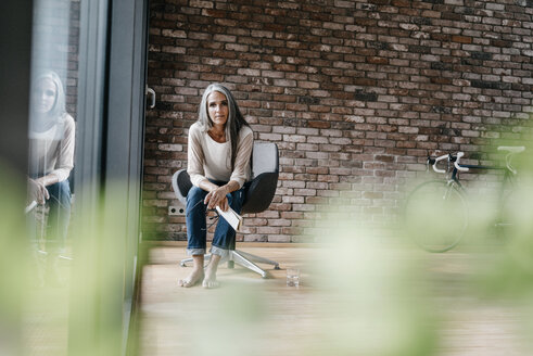 Frau mit langen grauen Haaren sitzt auf einem Stuhl am Fenster - KNSF00479