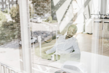 Smiling businessman in office behind windowpane - KNSF00511