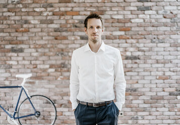 Portrait of confident businessman in front of brick wall - KNSF00517