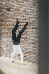 Geschäftsmann macht einen Handstand vor einer Ziegelmauer - KNSF00521