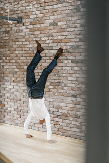 Geschäftsmann macht einen Handstand vor einer Ziegelmauer - KNSF00521