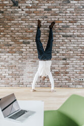 Businessman doing a handstand in front of brick wall - KNSF00522