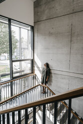 Frau mit langen grauen Haaren schaut im Treppenhaus aus dem Fenster - KNSF00527