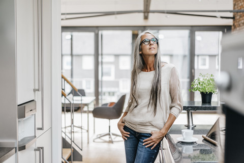 Woman with long grey hair in kitchen looking up stock photo