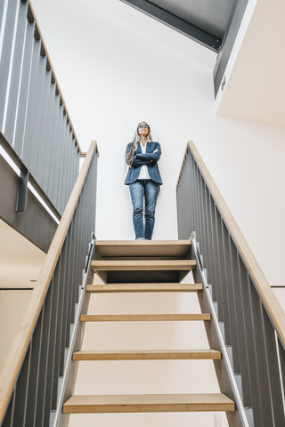 Selbstbewusste Geschäftsfrau mit langen grauen Haaren, die auf einer Treppe steht, lizenzfreies Stockfoto