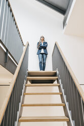 Selbstbewusste Geschäftsfrau mit langen grauen Haaren, die auf einer Treppe steht - KNSF00561