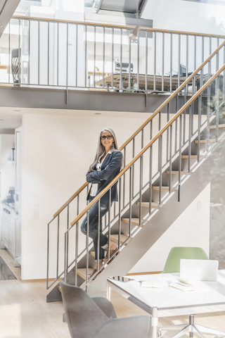 Lächelnde Geschäftsfrau mit langen grauen Haaren auf einer Treppe stehend, lizenzfreies Stockfoto