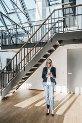 Businesswoman with long grey hair using tablet in a loft - KNSF00576