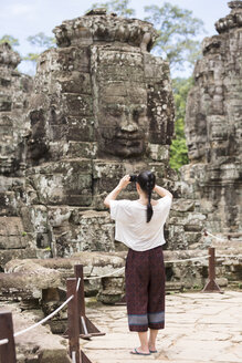 Kambodscha, Siem Reap, Angkor Thom, Rückenansicht eines Touristen beim Fotografieren des Bayon-Tempels - MADF01216