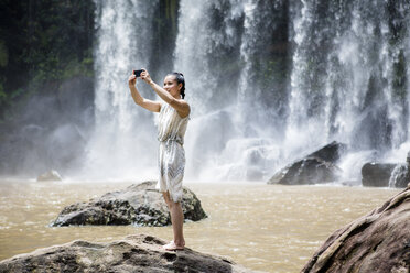 Kambodscha, Nationalpark Phnom Kulen, junge Frau macht Selfie mit Smartphone vor den Wasserfällen - MADF01226