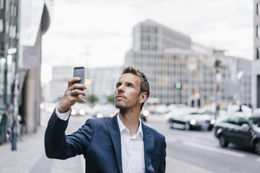 Deutschland, Berlin, Geschäftsmann fotografiert mit Smartphone - KNSF00591