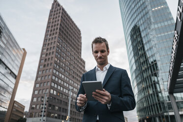 Germany, Berlin, smiling businessman standing at Potsdamer Platz looking at tablet - KNSF00598