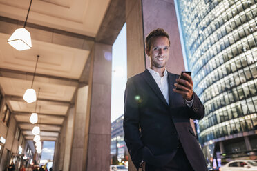 Germany, Berlin, portrait of smiling businessman at Potsdamer Platz in the evening - KNSF00608