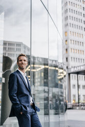 Portrait of confident businessman leaning against glass facade - KNSF00623