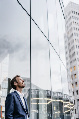 Geschäftsmann lehnt an Glasfassade, lizenzfreies Stockfoto