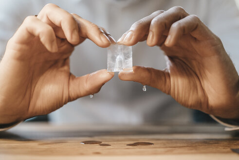 Hands of man holding melting ice cube - KNSF00630