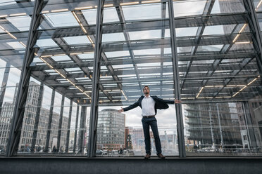 Germany, Berlin, businessman with arms outstretched standing in front of glass pane - KNSF00638