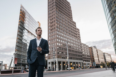 Deutschland, Berlin, Geschäftsmann mit Smartphone, stehend am Potsdamer Platz - KNSF00642