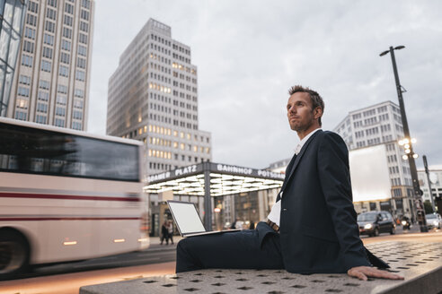 Deutschland, Berlin, Potsdamer Platz, Geschäftsmann auf Bank sitzend mit Laptop am Abend - KNSF00647