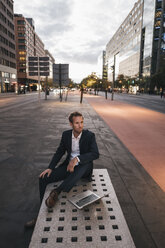 Deutschland, Berlin, Potsdamer Platz, Geschäftsmann auf Bank sitzend mit Laptop am Abend - KNSF00648