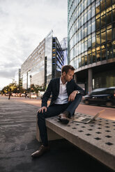 Germany, Berlin, Potsdamer Platz, businessman sitting on bench using laptop in the evening - KNSF00649