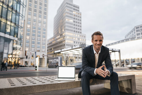 Deutschland, Berlin, Potsdamer Platz, Porträt eines Geschäftsmannes auf einer Bank sitzend mit Laptop - KNSF00650