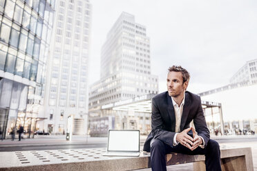 Germany, Berlin, Potsdamer Platz, portrait of businessman sitting on bench with laptop - KNSF00652