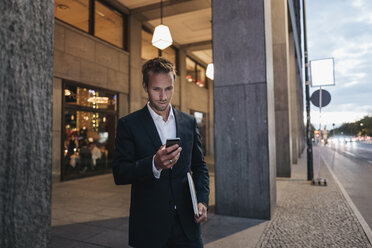 Businessman looking at smartphone in the evening - KNSF00654