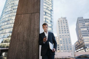 Deutschland, Berlin, Potsdamer Platz, Geschäftsmann schaut abends auf sein Smartphone - KNSF00655