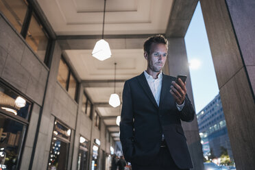 Germany, Berlin, portrait of businessman looking at his cell phone - KNSF00659