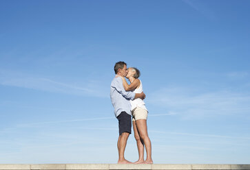 Senior Paar umarmt und küsst auf einer Mauer vor dem Himmel - HAPF01147